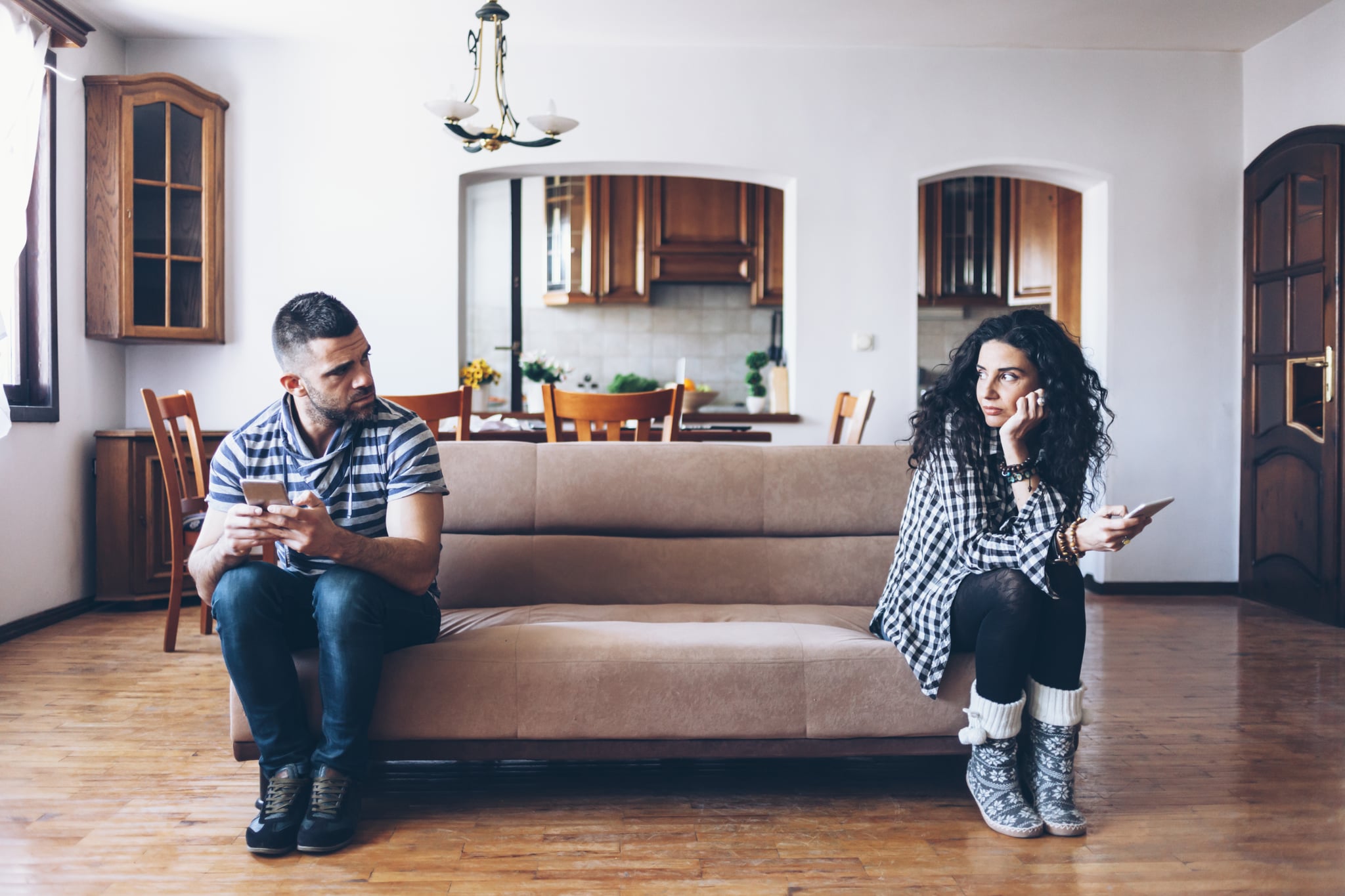 Couple in conflict sitting on sofa at home, using smart phones.