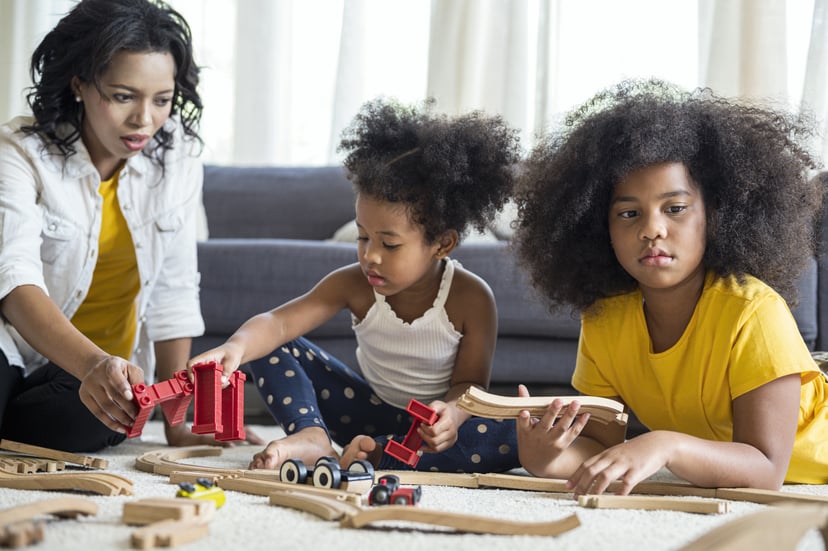 Cute girls entertaining with toy car near her sister on floor. Happy family spending time together in living room on weekend.
