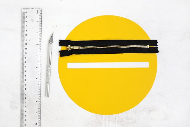 Designate one of the circles to be the back of your bag, and cut a slit that is 1/2" wide and 7" long down the middle of the circle. Try to find a zipper that is exactly 7" long if you can, but if you can't find one, you can use wire cutters and scissors to trim the zipper down to size (the wire cutters are to cut through the metal zipper section more easily). You can also adjust the length of the window you cut to accommodate a different size zipper.
Use the fabric glue to glue the zipper under the cutout so that the zipper fits perfectly in the window.