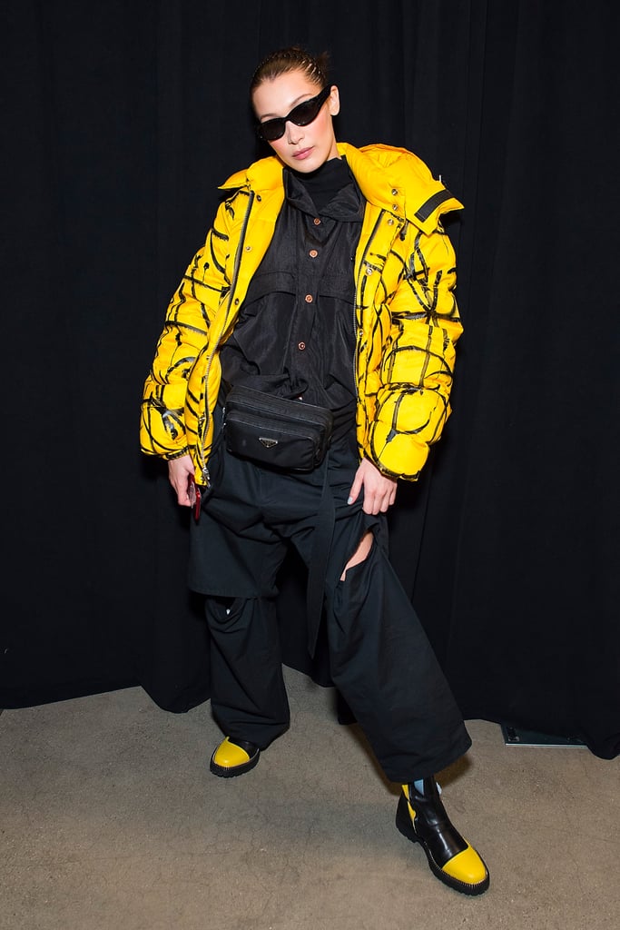 Posing backstage at Prabal Gurung's show wearing a neon yellow puffer, jumpsuit, and black and yellow boots by A.F. Vandevorst. She styled her look with a Prada waist bag.