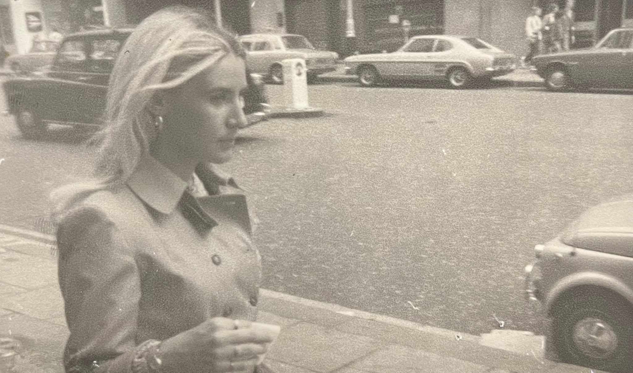 Woman in a trench coat walking down a sidewalk in 1971 London