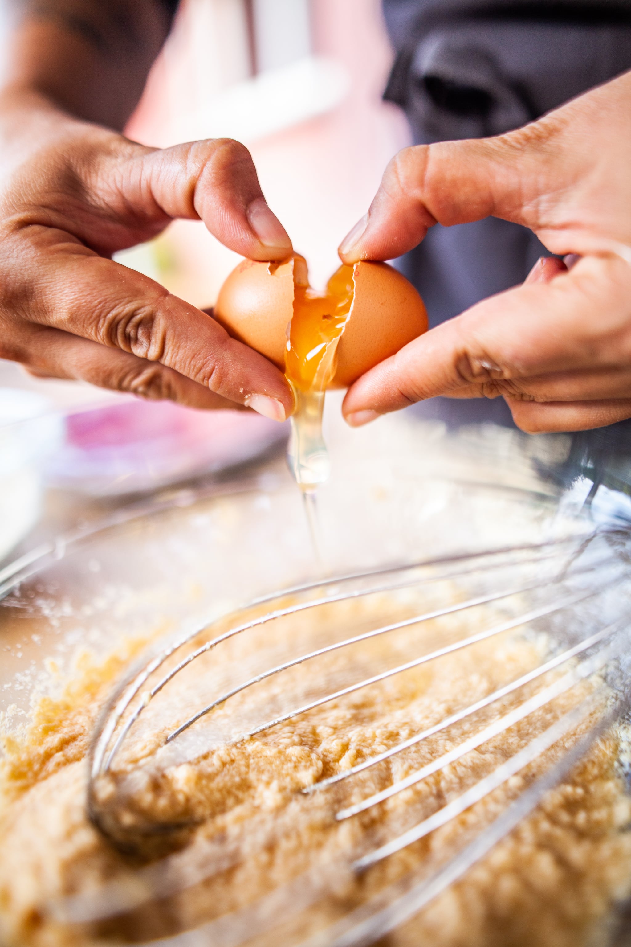 Cette photographie présente une personne en train de cuisiner, casser un œuf dans une préparation sucrée pour la réalisation d'un gâteau.