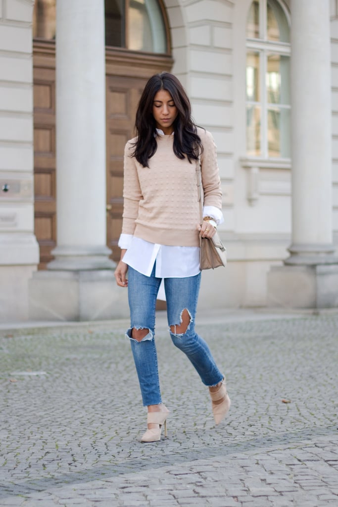 A blush sweater layered over a white shirt, jeans, and matching heels.