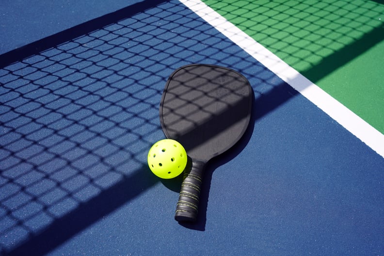 Pickleball paddle with ball on court with net shadow.