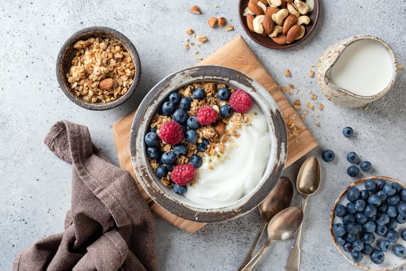 Greek yogurt granola bowl with blueberries and raspberries on wooden board.