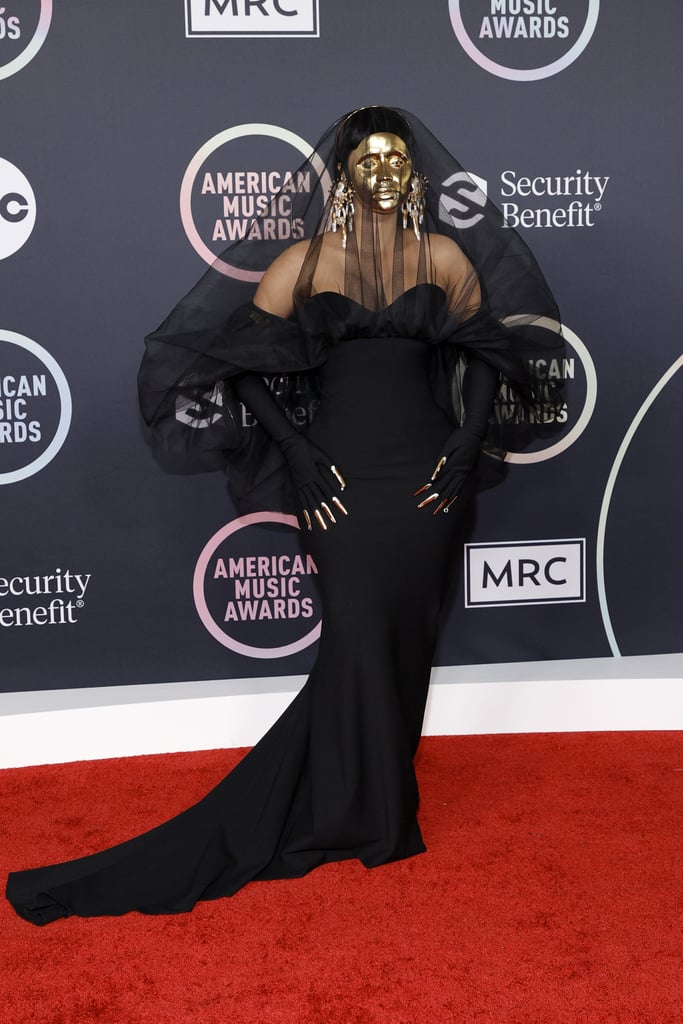 Cardi B walked the red carpet in a black Schiaparelli gown, matching veil, and gold face mask.