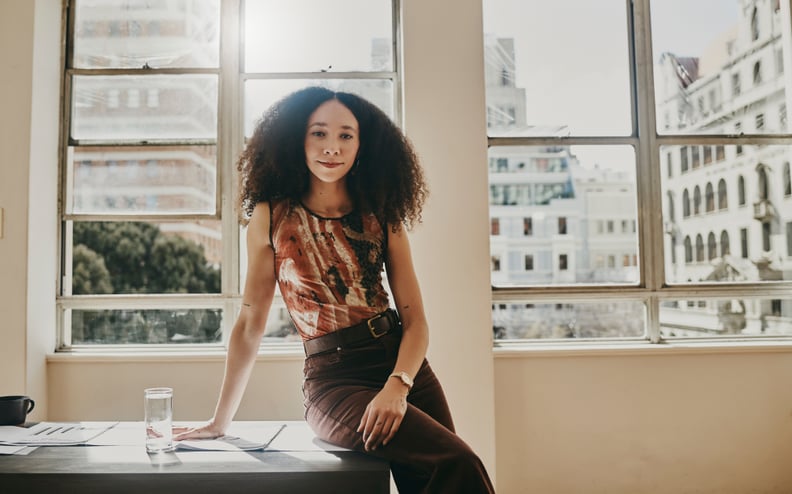 Woman in office sitting on desk and looking at camera