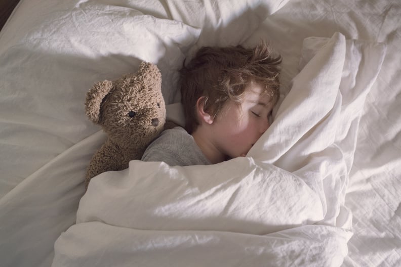 A boy sleeping alone in his parent's bed with his teddy bear.