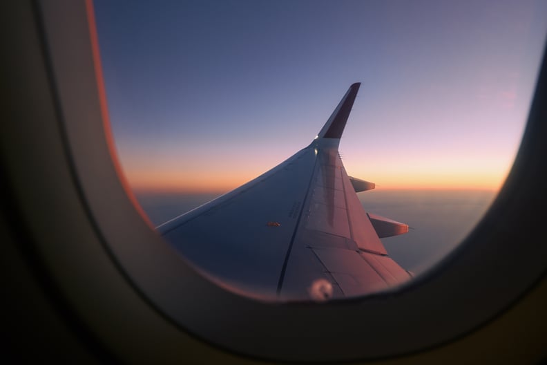 View through airplane window flight above clouds at colorful sunset.