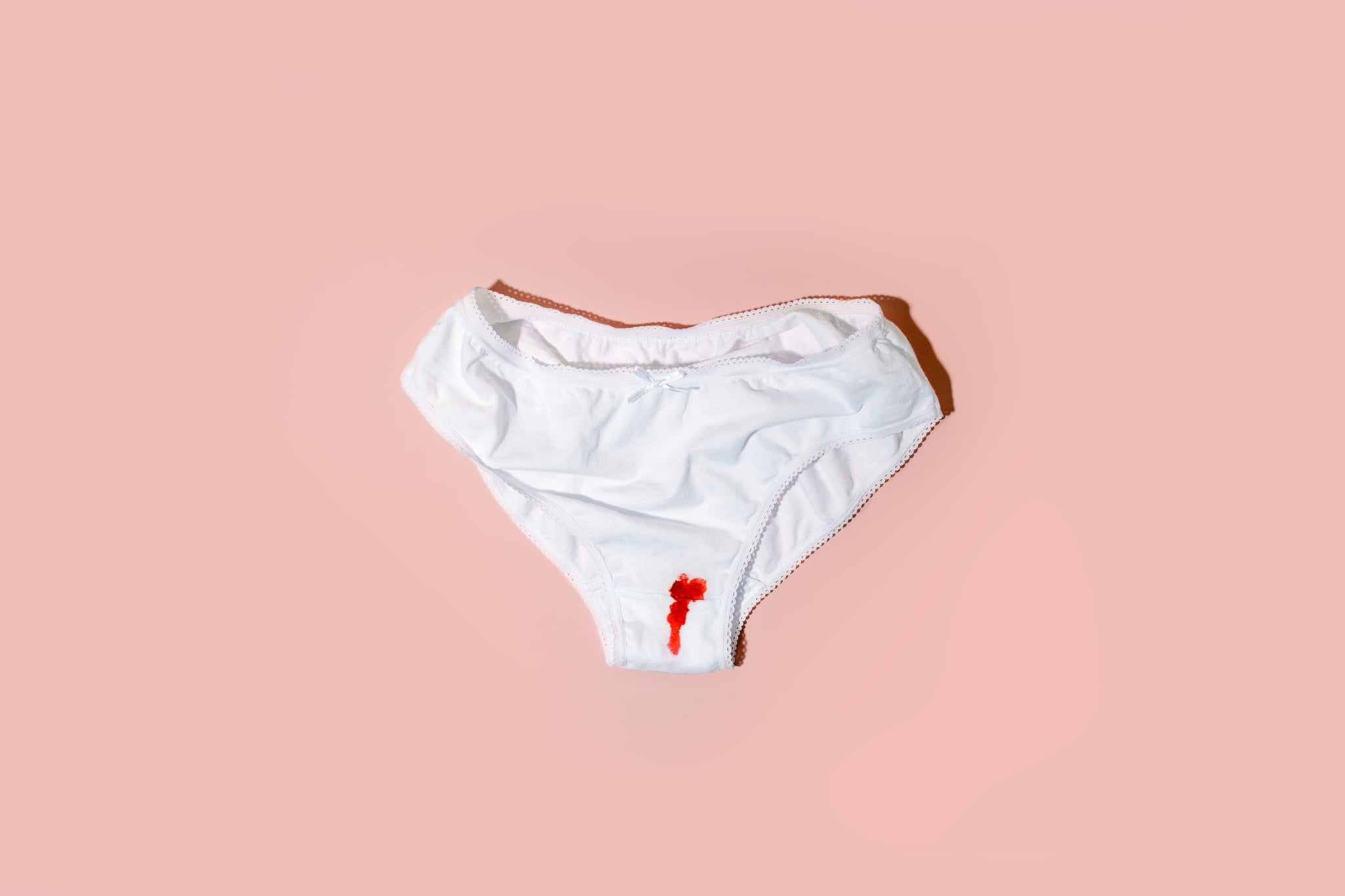 White cotton panties for with traces of red blood on a pink backdrop.