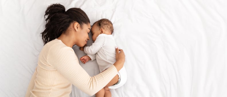 非洲母亲拥抱睡觉的婴儿躺在床上室内,俯拍。爱妈妈和蹒跚学步的婴儿小睡休息白天睡觉。全景,自由空间的文本