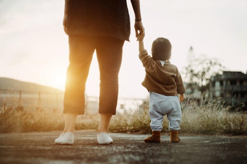 Low section of mother holding baby daughter's hand  walking in the park and enjoying the beautiful sunset