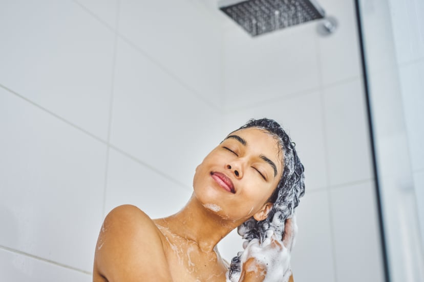 Shot of an attractive young woman washing her hair with shampoo in the shower at home