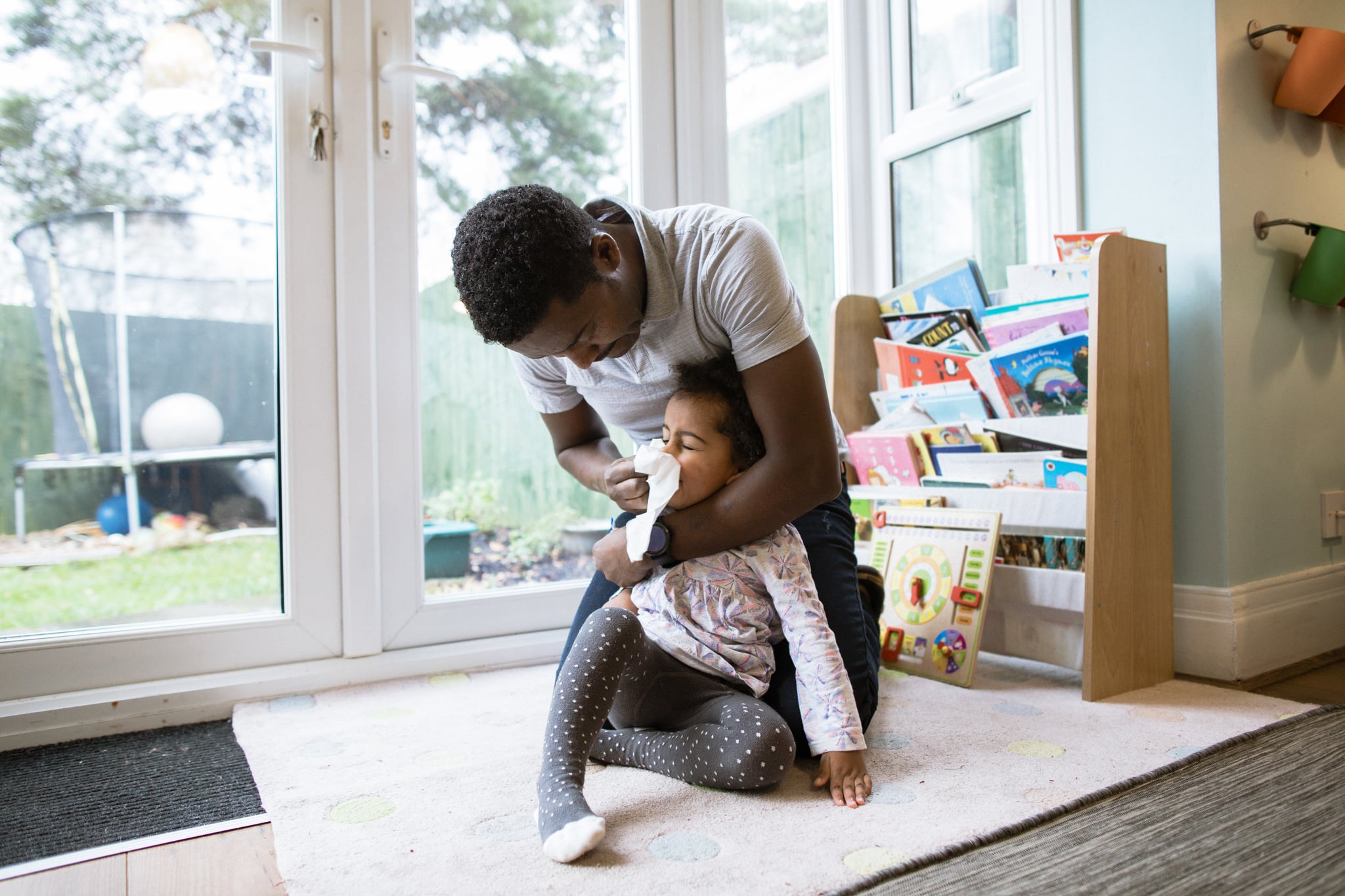 A young mixed race girl getting her Ethiopian dad, to wipe her runny nose whilst playing together at home.