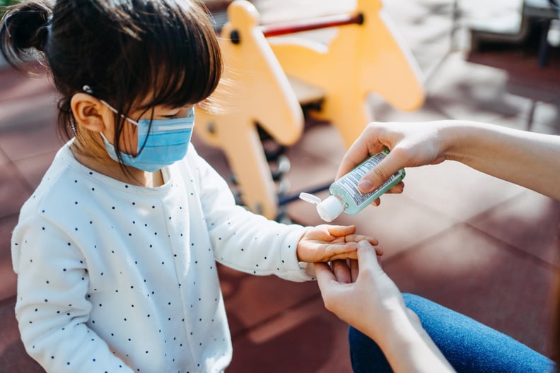 Young mother squeezing hand sanitizer onto little daughter's hand in the playground to prevent the spread of viruses