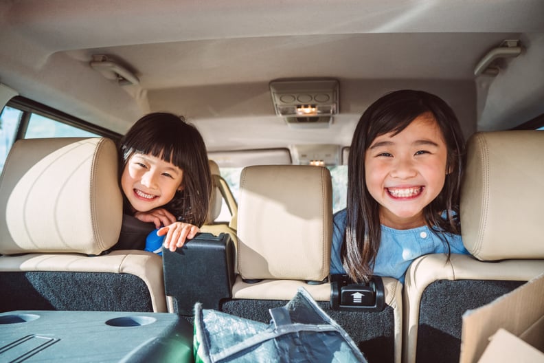 Lovely little sister looking out from an opened car trunk joyfully while resting in a road trip.