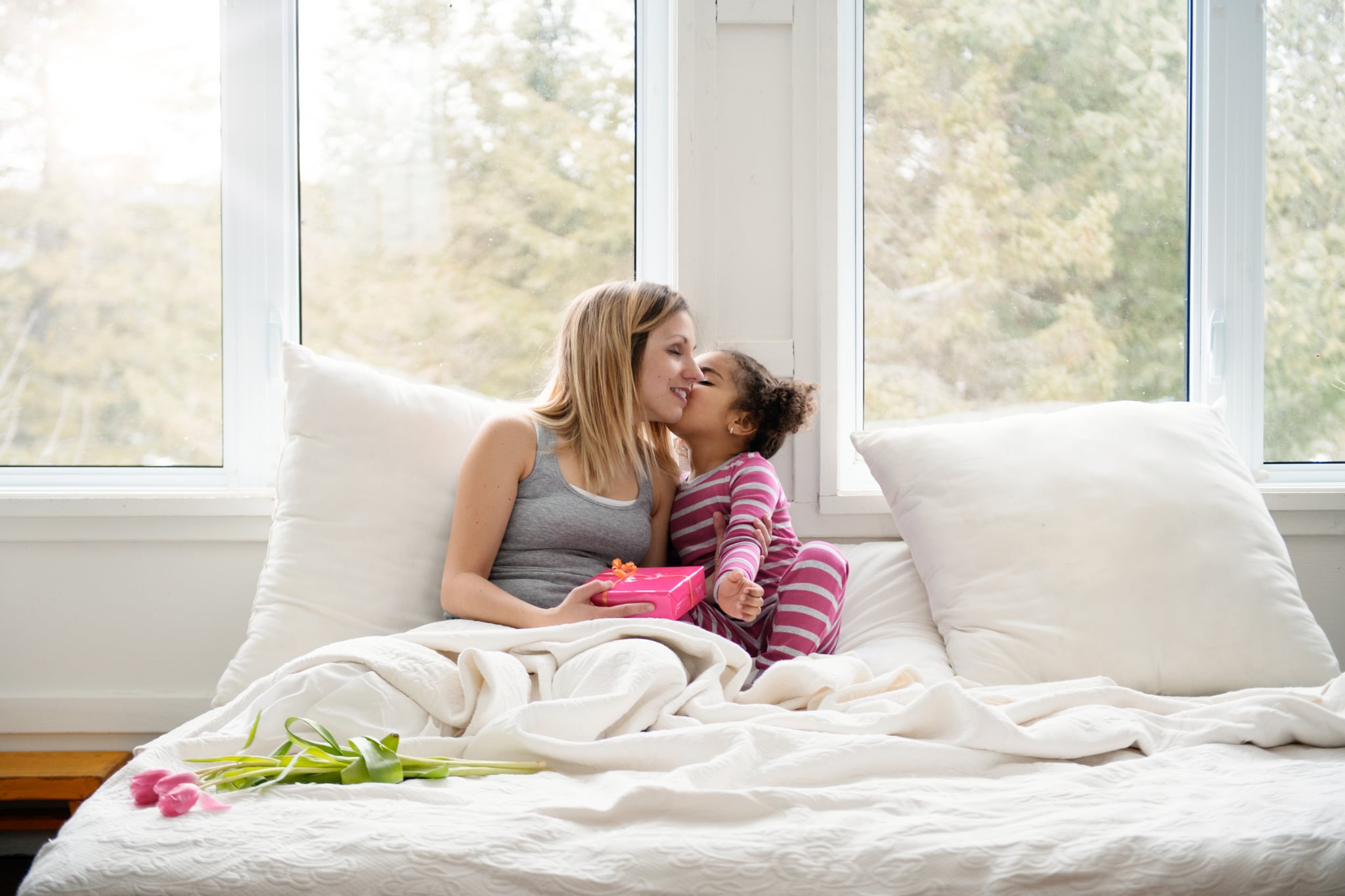 Sweet little mixed race girl of 4 years old old brings gift to bed to her mother during the mother's day. SHe is very proud to do that.  SHe wear pink pyjama. Photo can be use for Valentine's day, father's day, birthday. Photo was taken in Quebec Canada.