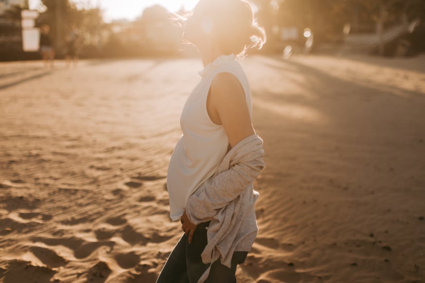 Photo of a young woman enjoying pregnancy while walking down the beach on sunset