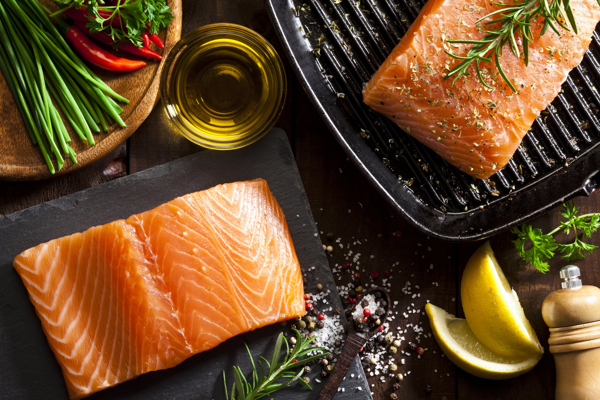 Top view of two raw salmon steaks ready for cooking. Some ingredients for cooking salmon like salt, pepper, rosemary, chive, lime and olive oil are all around the frame. DSRL studio photo taken with Canon EOS 5D Mk II and Canon EF 100mm f/2.8L Macro IS USM