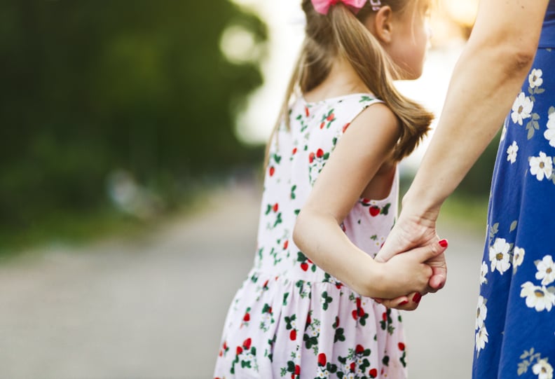 Mother and daughter are holding hands outdoors in summer.