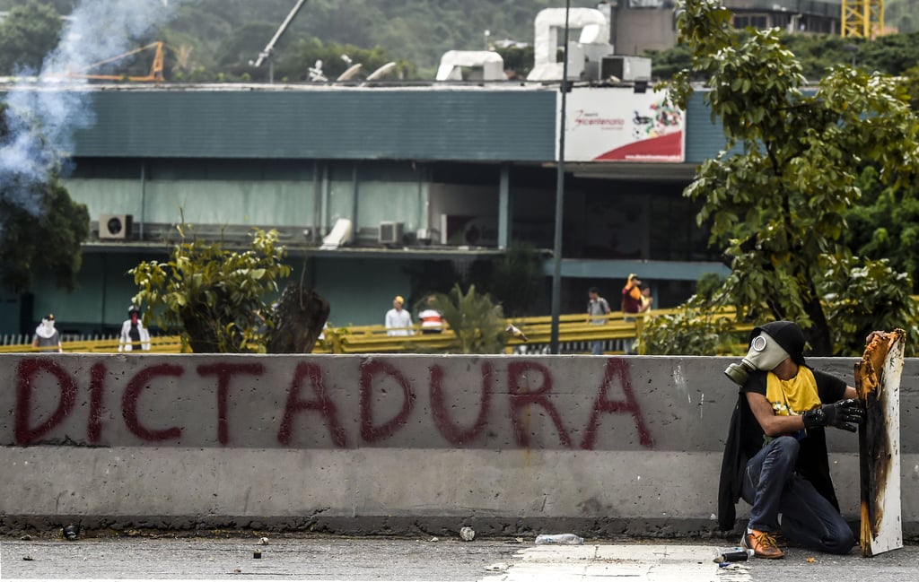 A man sits next to graffiti that reads "dictatorship."