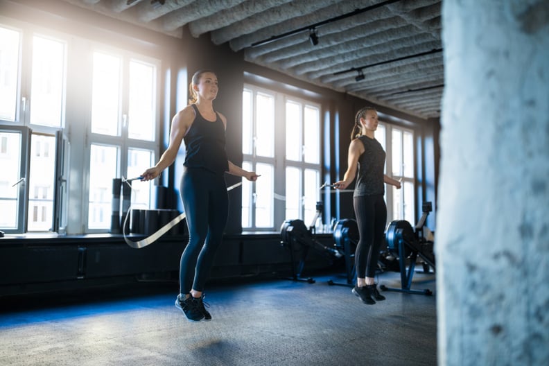 Young women doing workout with jump ropes in gym. Determined female athletes are exercising at health club. They are in sports clothing.