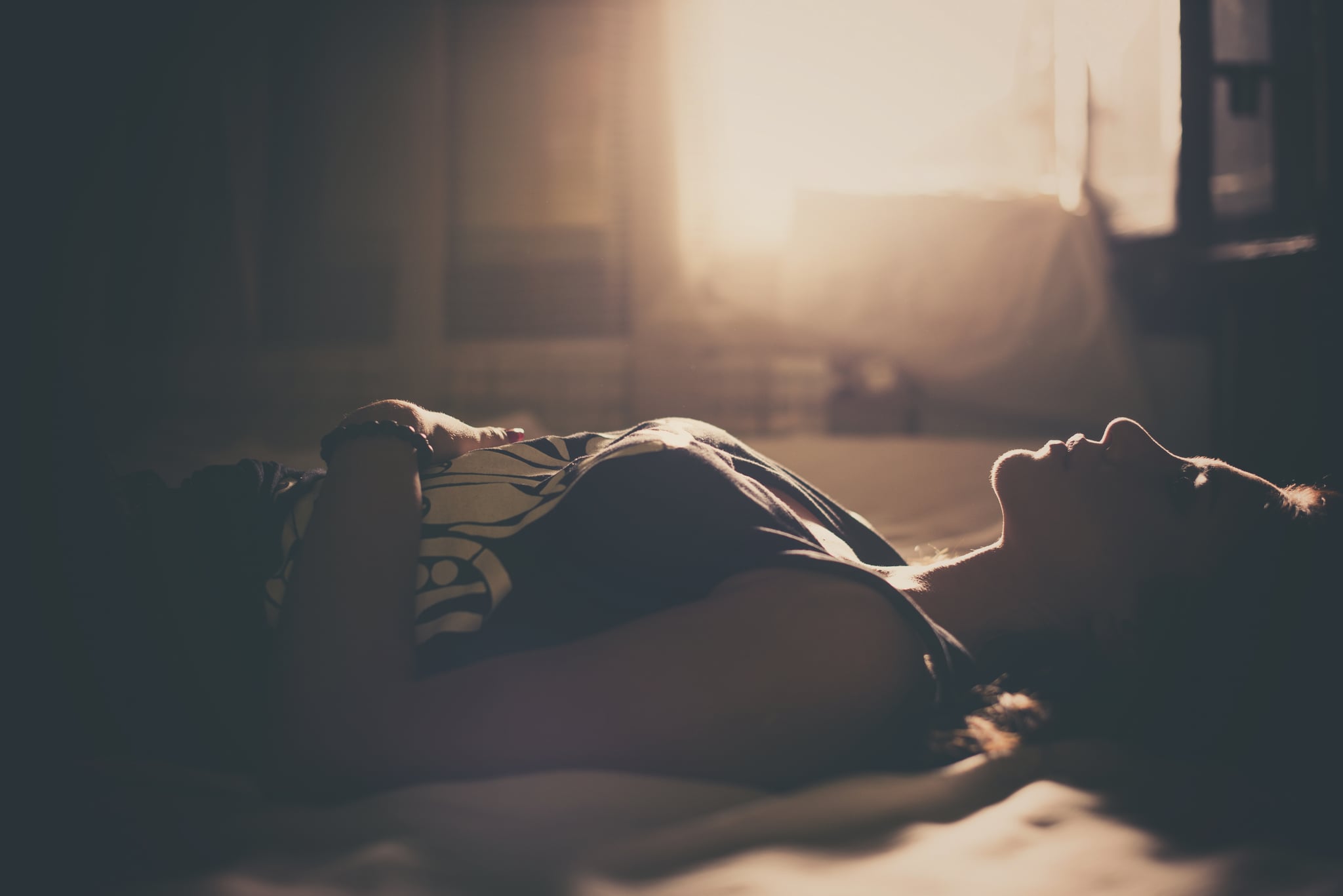 Sad girl in bed, backlit scene. Desaturated image.