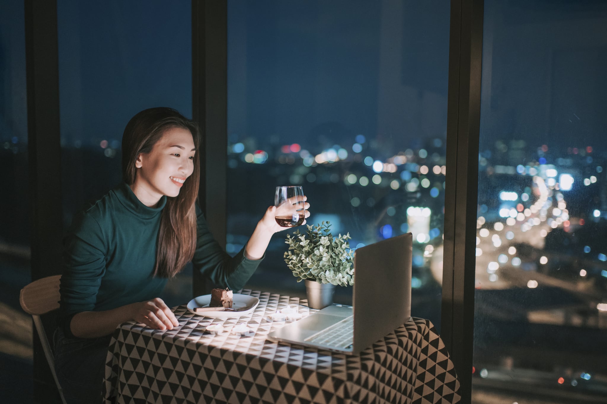 an asian chinese beautiful young lady having dessert in her apartment during magic hour, dusk and talking to her boyfriend thru internet using her laptop