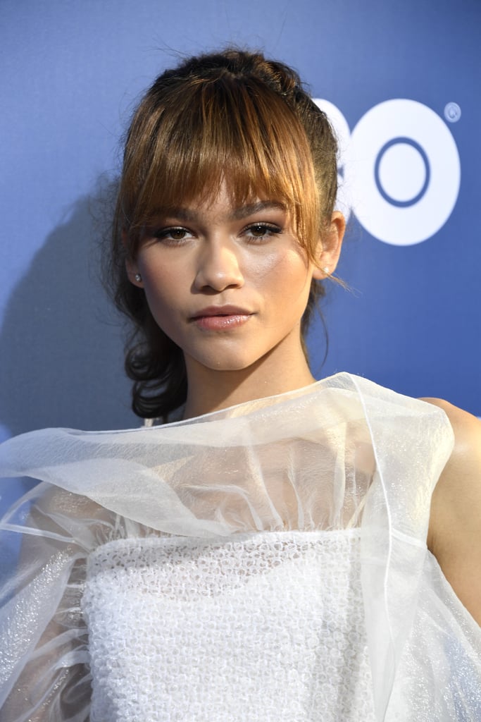 Real-life Disney princess Zendaya is blessing us not only with a new show to binge-watch but also a new hair look we are seriously considering copying. The actress debuted eye-grazing bangs with longer sides at HBO's Euphoria premiere (in which she stars) — and wore her hair up in a ponytail to show them off. She paired her new hair with soft peach makeup on her eyes and cheeks and a glossy lip. If you've been considering your own Summer bangs, consider taking a photo of Zendaya's chic style with you to your hairstylist for inspiration. Check out her bangs from every angle, ahead.