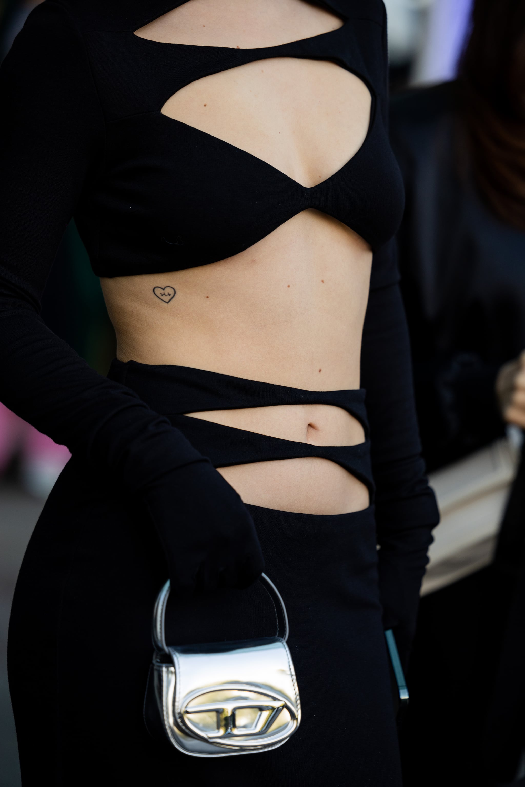 ALMATY, KAZAKHSTAN - MAY 04: A guest with heart tattoo wears black cut out dress, silver Diesel bag, gloves at VISA Fashion Week Almaty Season VII (Autumn/Winter 2024) on May 04, 2023 in Almaty, Kazakhstan. (Photo by Christian Vierig/Getty Images)