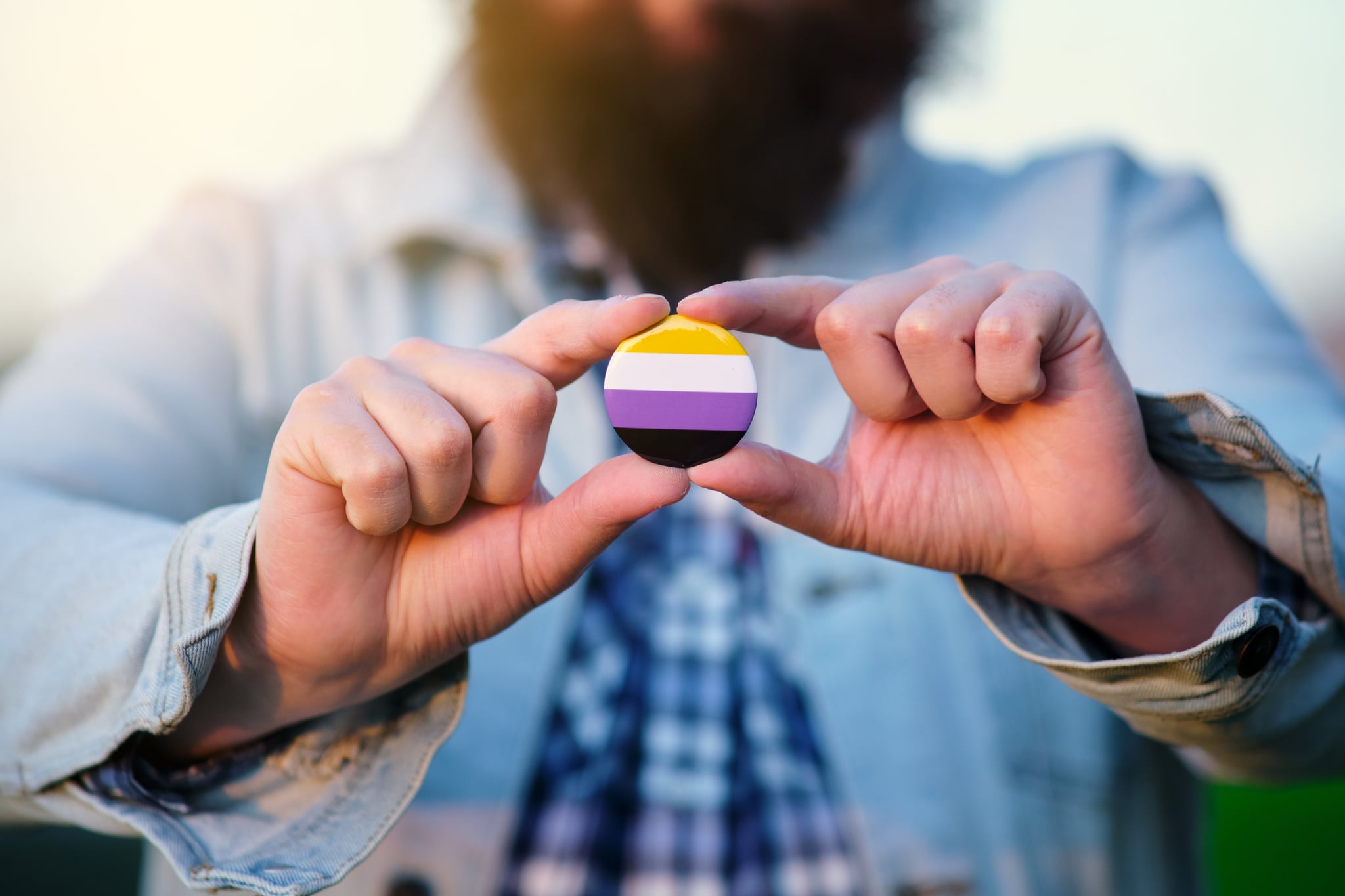 An unrecognisable person holding and showing a pin with non binary colours flag