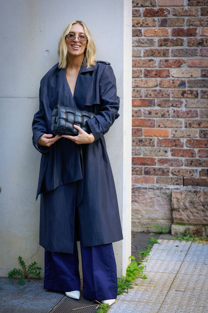 Phoebe Burgess wore a navy trench, brown tinted sunglasses, navy wide pants and Bottega Veneta clutch.