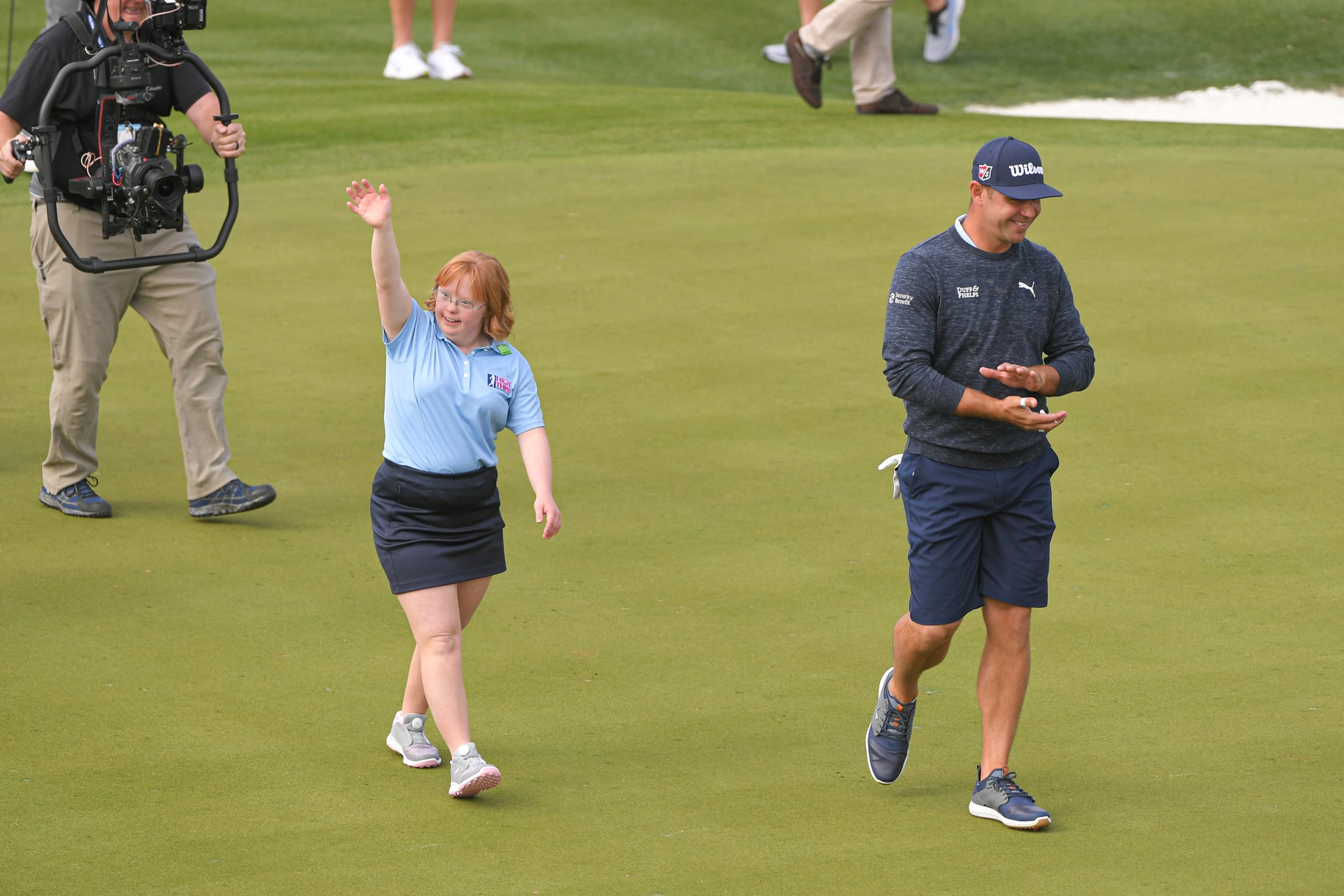 SCOTTSDALE, AZ - JANUARY 29: Amy Bockerstette waves while walking with Gary Woodland on the 16th green prior to the Waste Management Phoenix Open at TPC Scottsdale on January 29, 2020 in Scottsdale, Arizona. (Photo by Ben Jared/PGA TOUR via Getty Images)