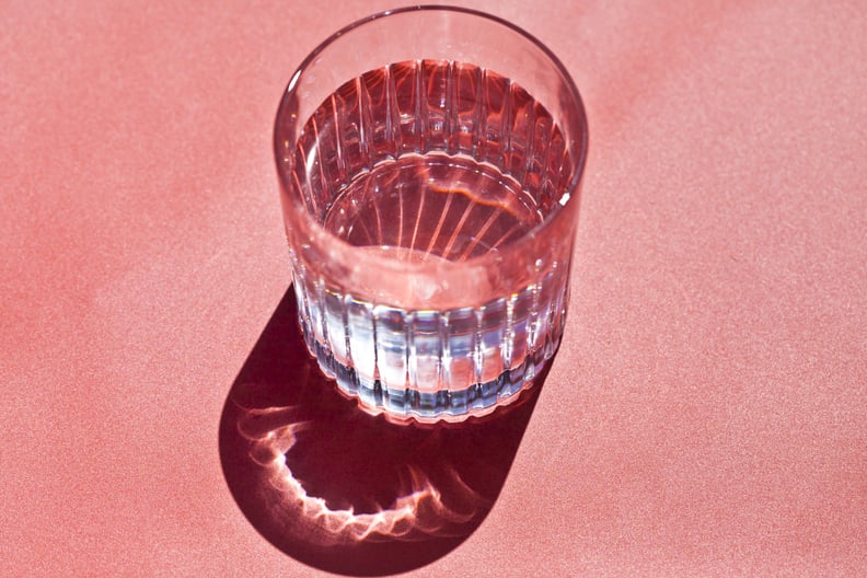 Close-up of a glass of water shining in the sunlight on a pink background.