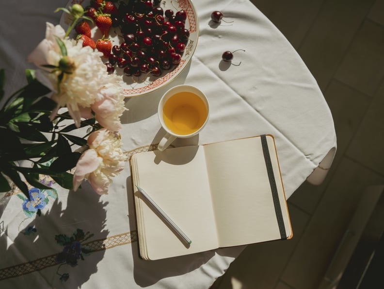 open journal beside a cup of tea and flowers