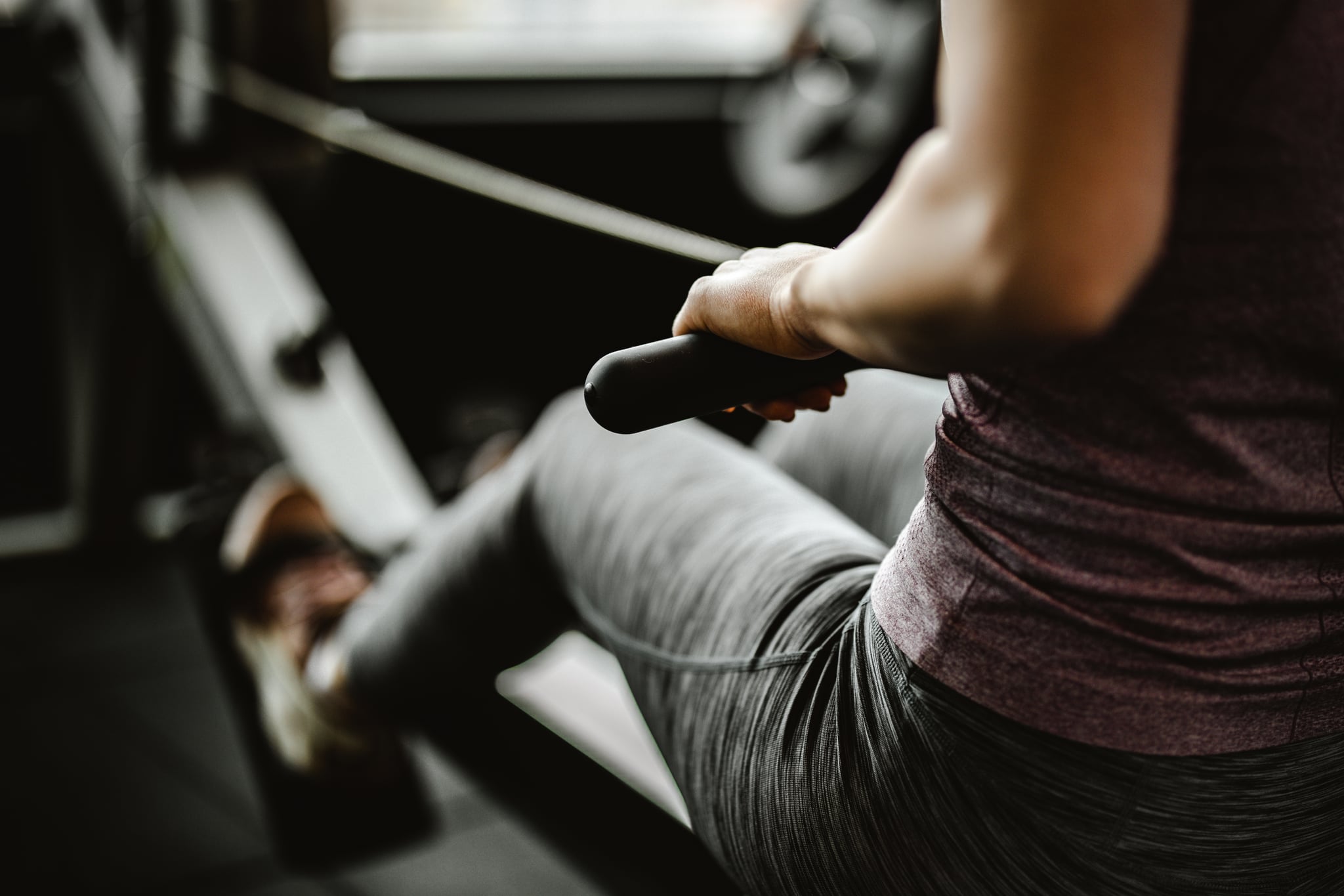 Close up of unrecognizable female athlete having sports training on rowing machine in a gym.