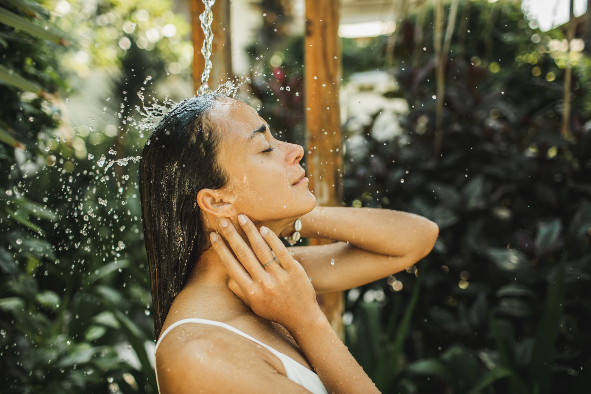 A woman in white swimsuit relaxing and refreshing under an outdoor shower.