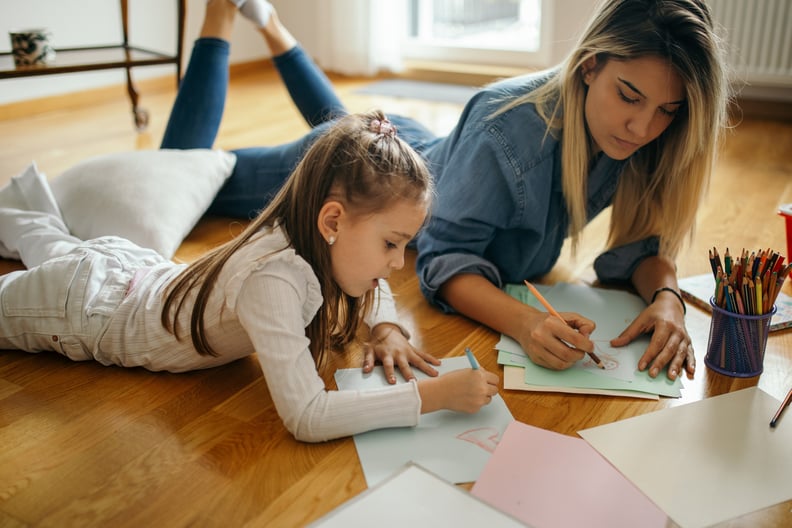 Young woman and little girl are playing and and drawing and coloring together in their living room while lying on floor. Woman is girl's aunt and nanny. They are beautiful and playful