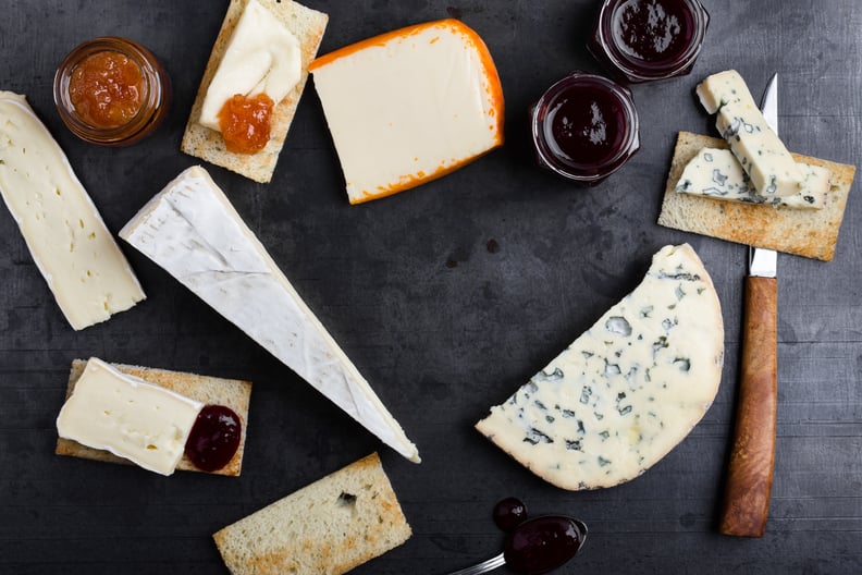 Various types of French cheese with jam over gray background viewed from above. Creamy Saint Paulin cheese, brie, Fourme d'Ambert blue cheese