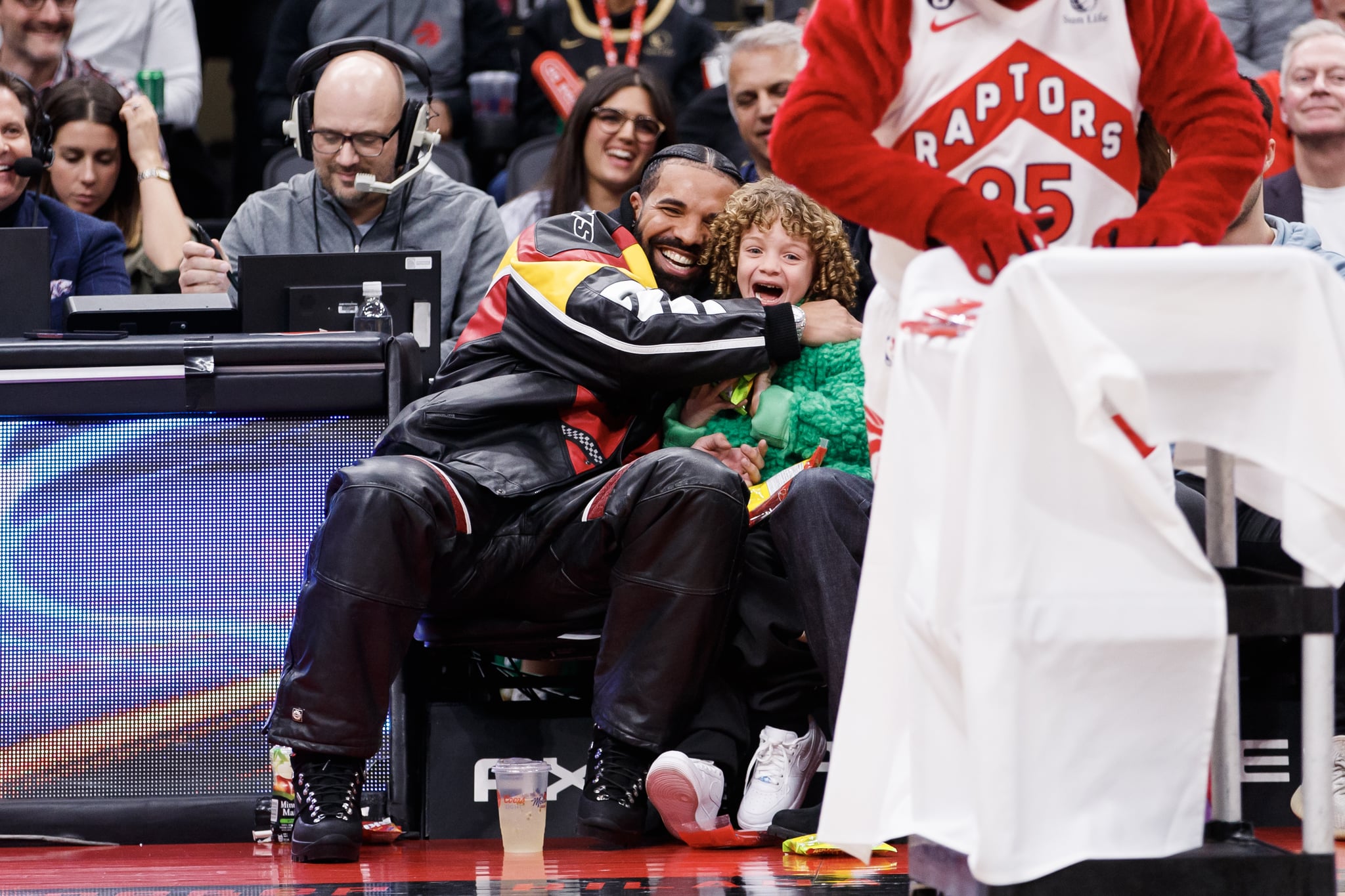 TORONTO, ON - DECEMBER 27: Rapper Drake embraces his son Adonis as the Raptor mascot brings over candy for him during the first half of the NBA game between the Toronto Raptors and the LA Clippers at Scotiabank Arena on December 27, 2022 in Toronto, Canada. Photo by Cole Burston/Getty Images)