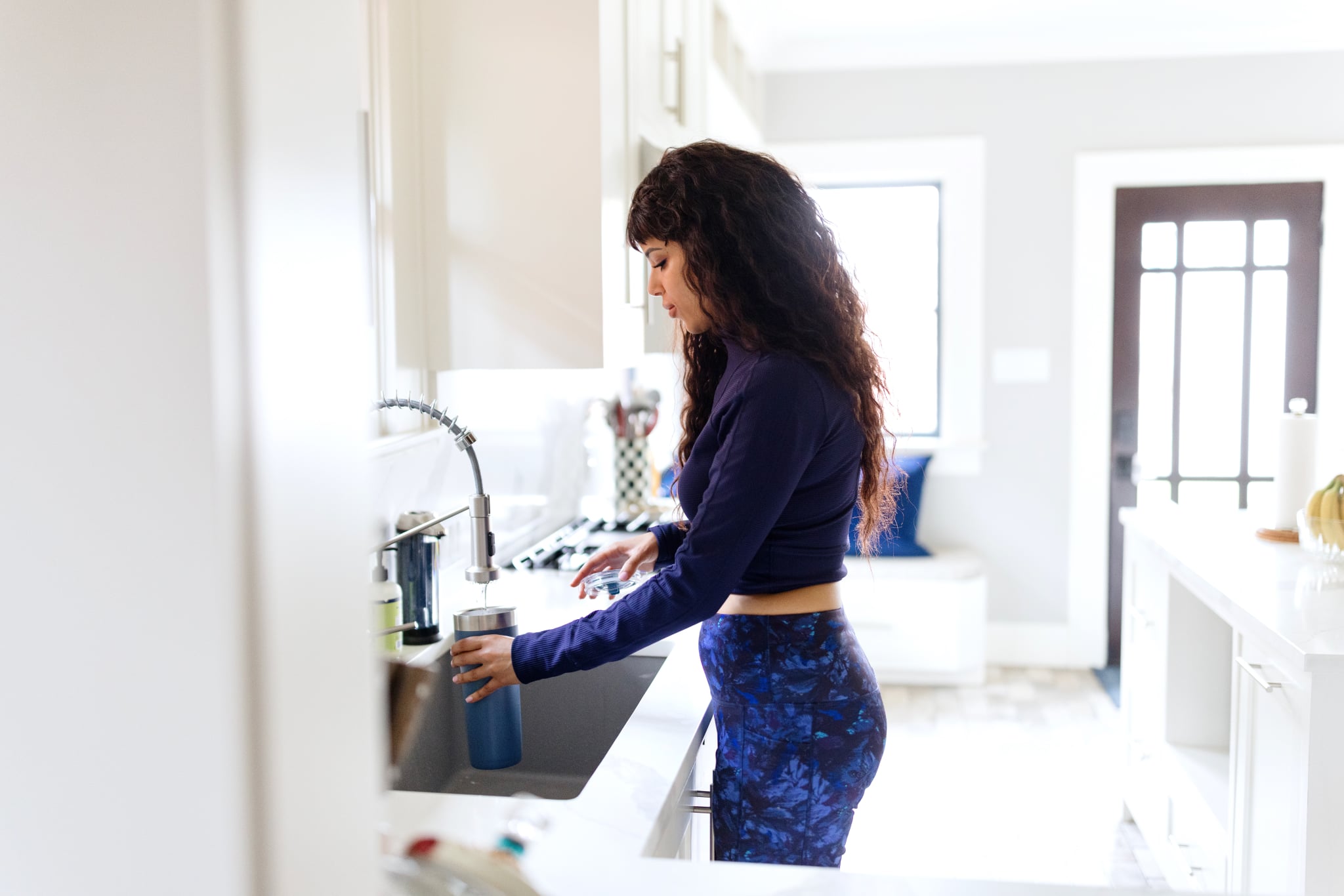 Woman pours water in the water bottle while wearing activewear.