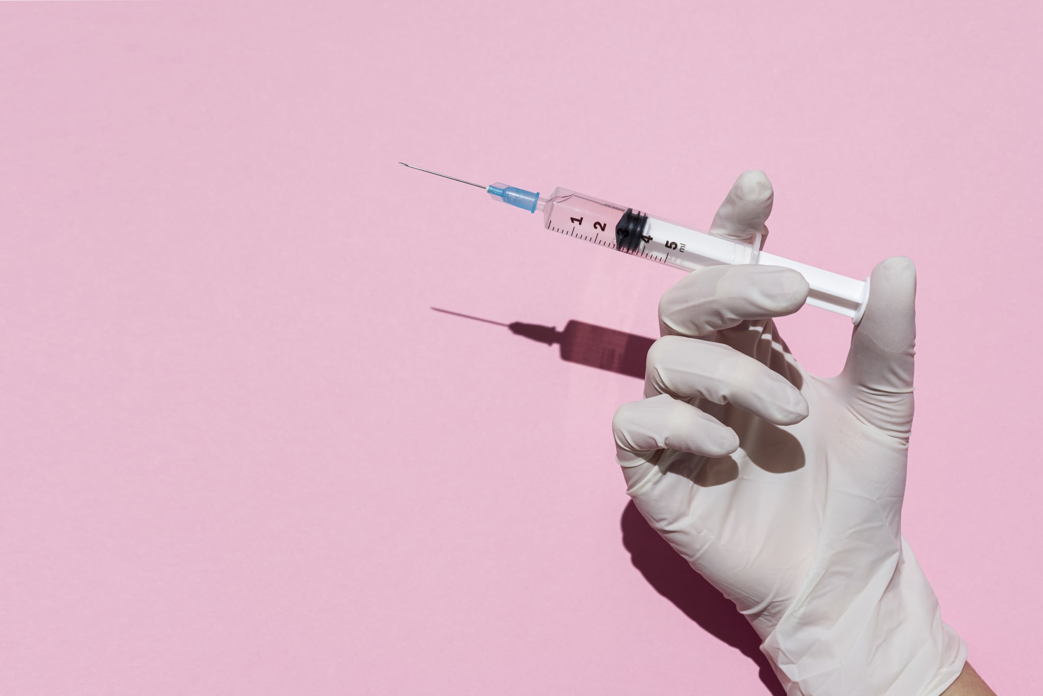 Woman's hand holding syringe in plain pink background.Studio Shot