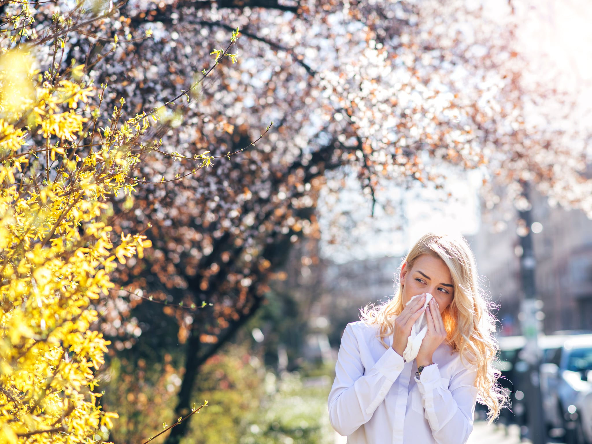 woman blowing her nose outside wondering if she has allergies or covid