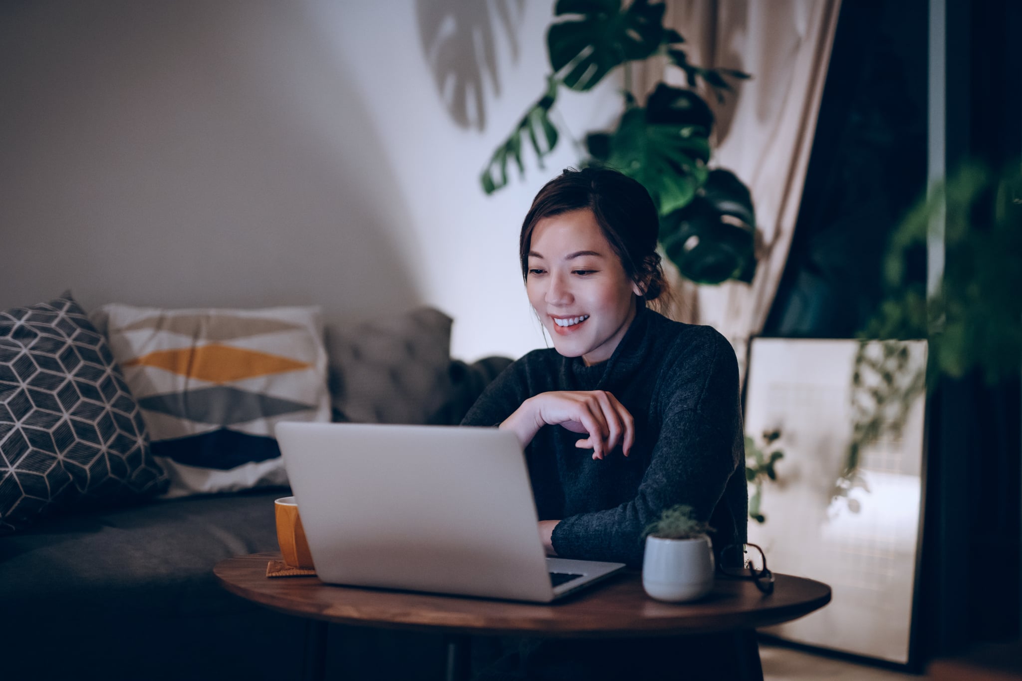 开朗的年轻亚洲女性在家里使用笔记本电脑直到深夜。生活方式与科技理念
