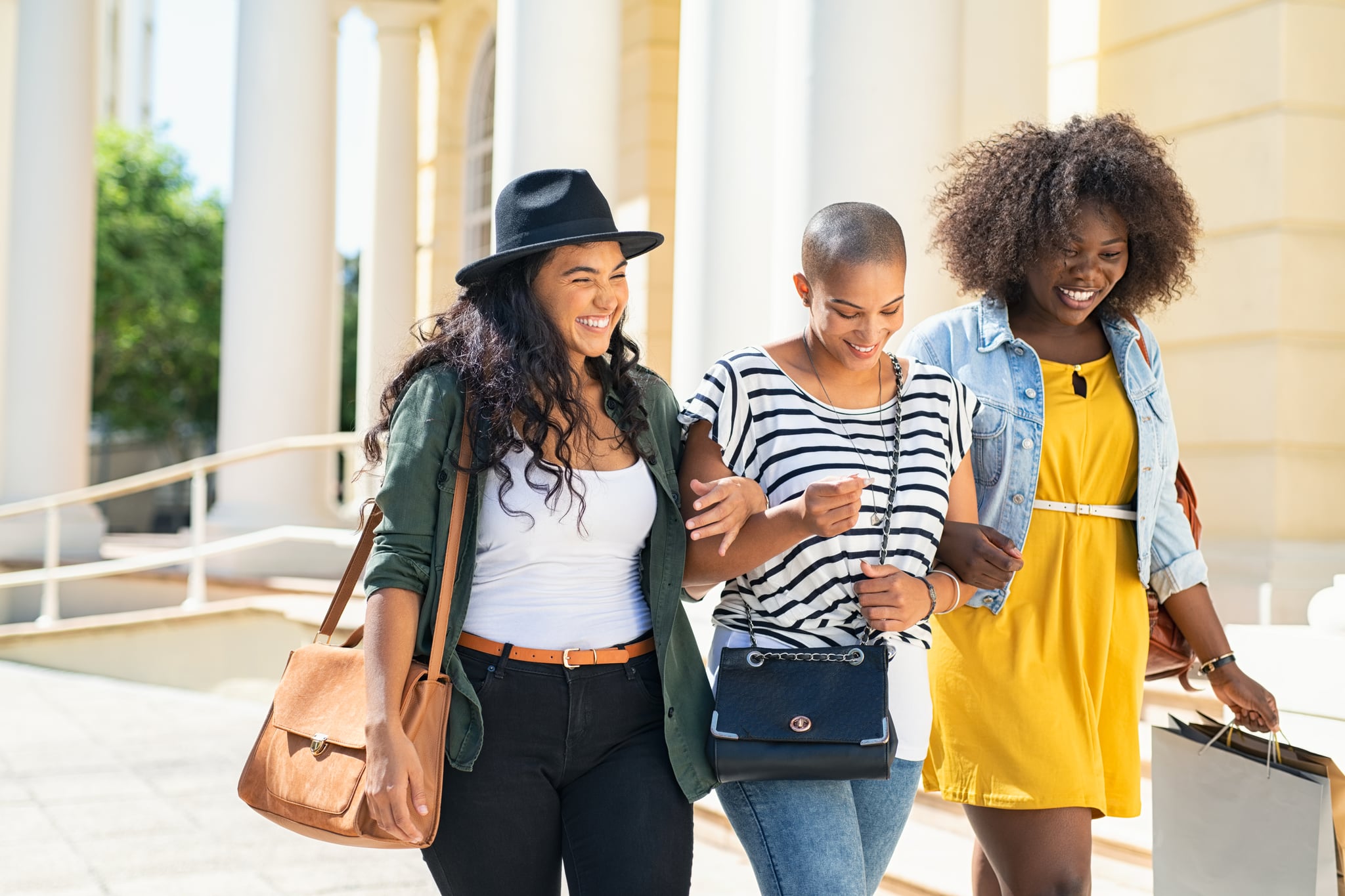 Group of three friends walking and holding shopping bags. Three happy young women walking in the city talking to each other while having fun on street. Multiethnic group of girls smiling with shopping bags outdoor.