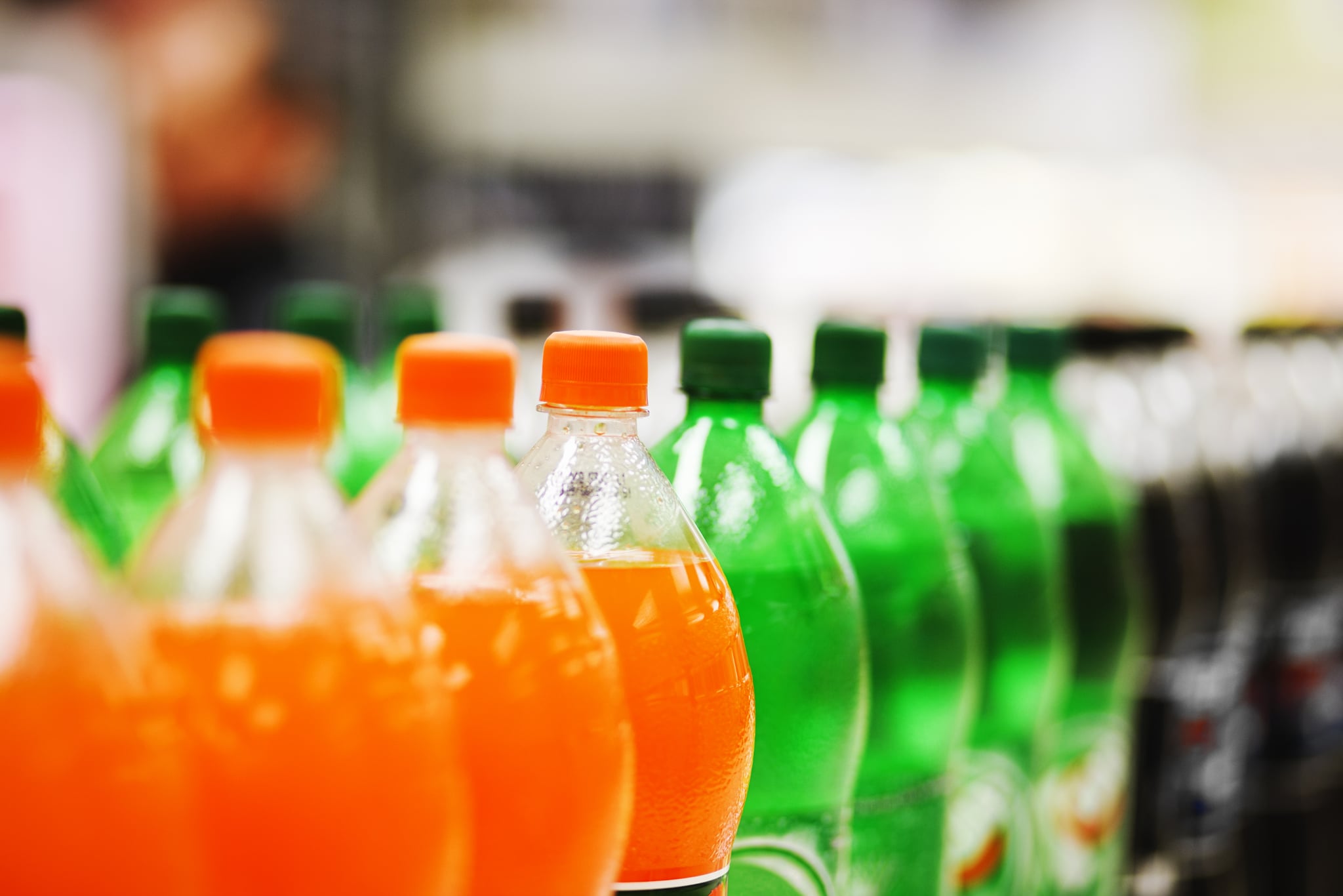 A long line of unbranded soda bottles in various flavours and colours, the focus on the centre of the line.