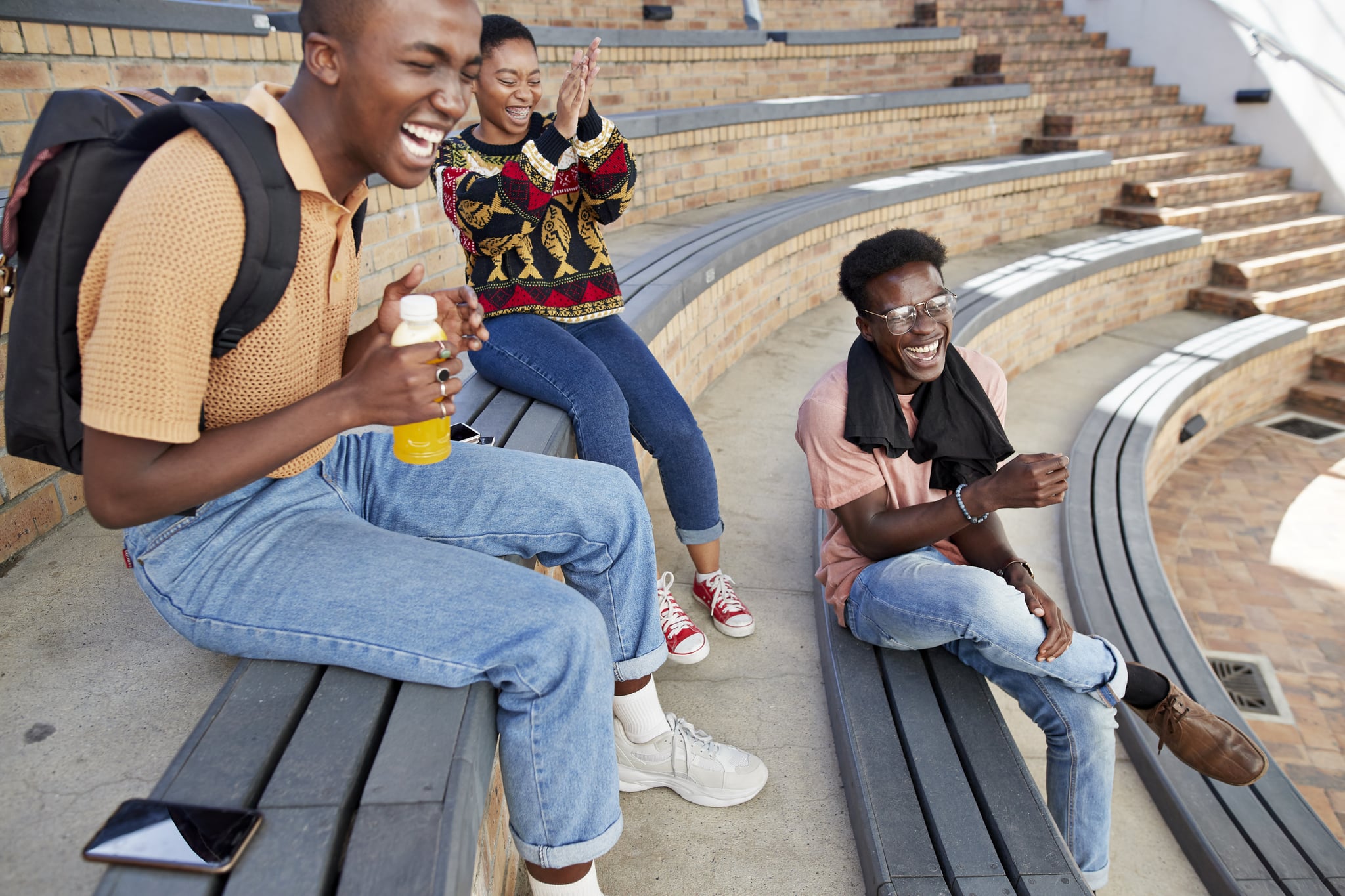 Cheerful young male and female friends enjoying on amphitheatre steps at university campus