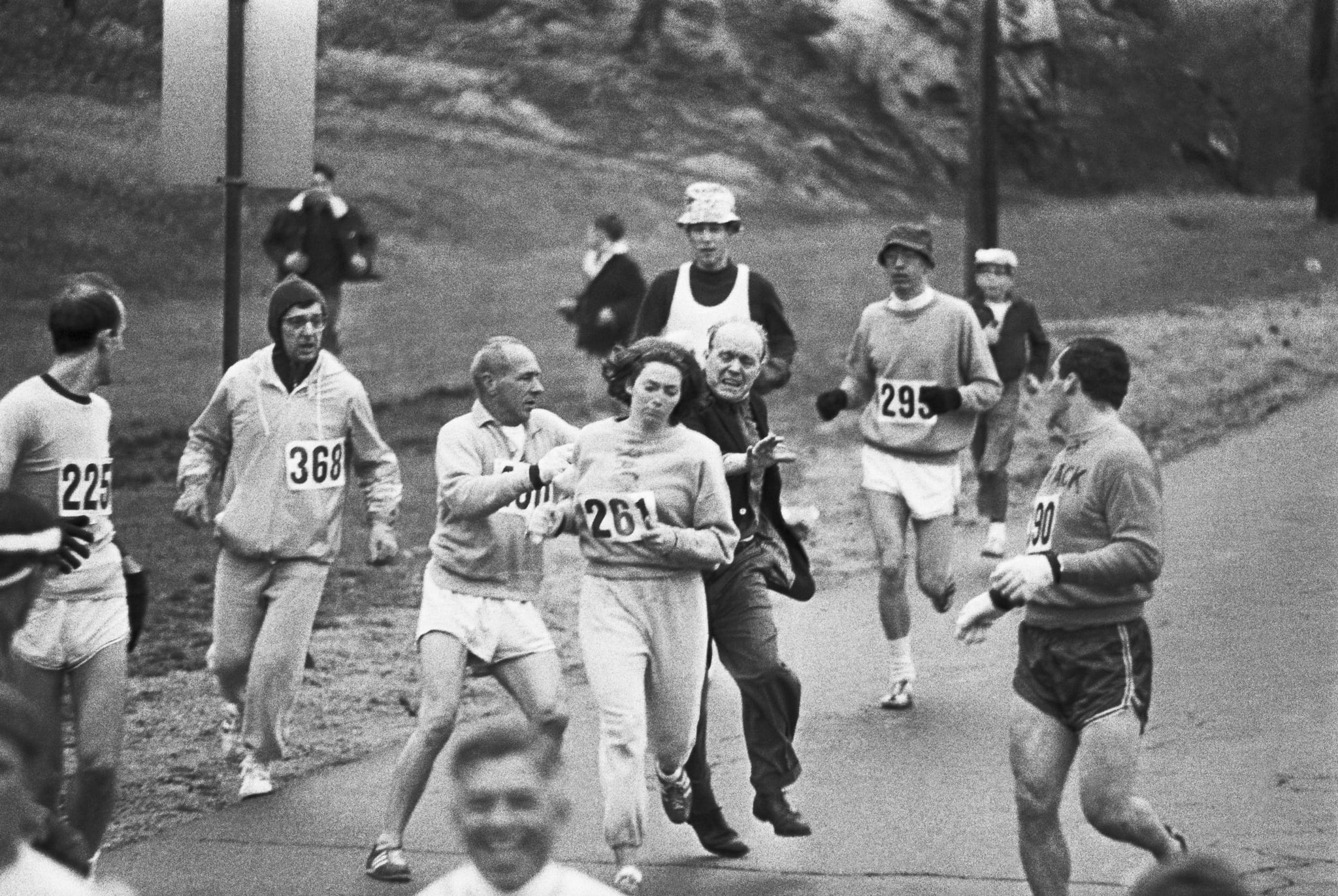 Trainer Jock Semple -- in street clothes -- enters the field of runners (left) to try to pull Kathy Switzer (261) out of the race. Male runners move in to form a protective curtain around female track hopeful until the protesting trainer is finally wedged out of the race