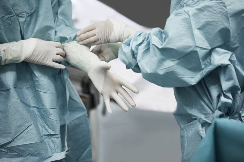 上腹部的女医生帮助外科医生戴上手套。医学的同事正在准备手术。他们是站在急诊室。