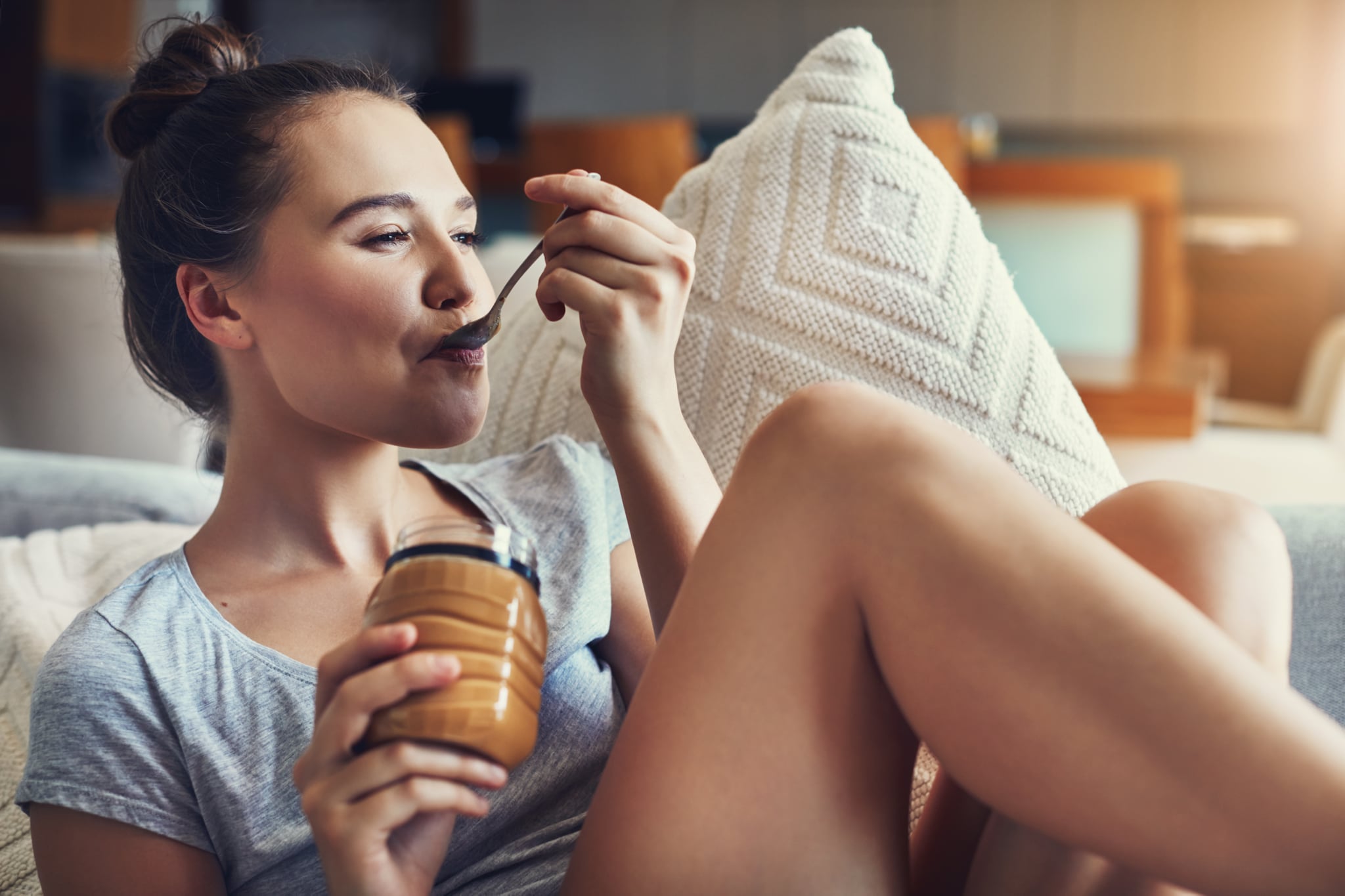 Shot of an attractive young woman eating peanut butter while relaxing on the sofa at home